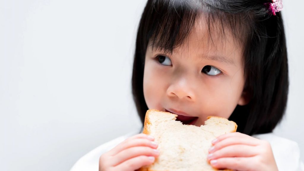 Bambina che mangia una fetta biscottata